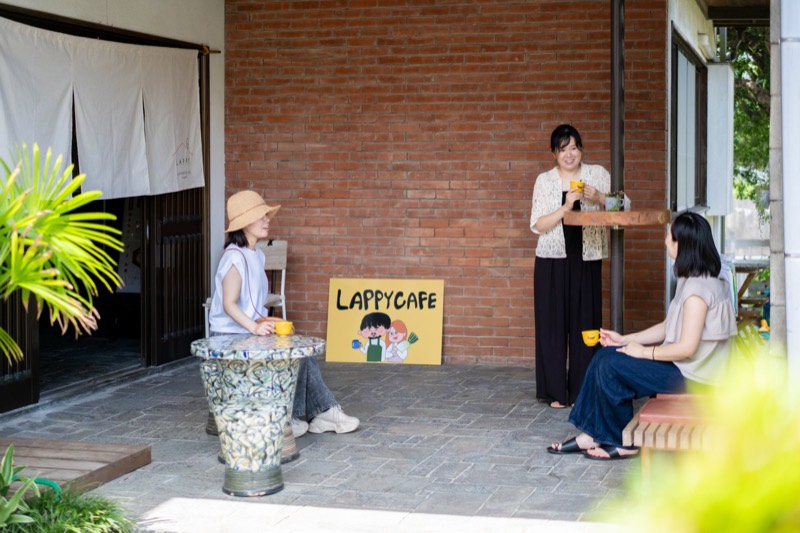建物の前のベンチとテーブルで、コーヒーを飲む人たち