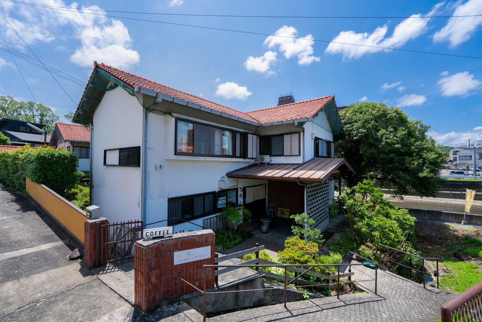 GUESTHOUSE LAPPYの建物。赤い瓦屋根の2階建てで、1階がLAPPY CAFE、2階がゲストハウスです。門の前に「COFFEE」の看板があります