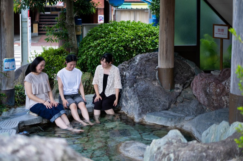 石で囲まれた足湯に、足をひたしてひと休みする3人