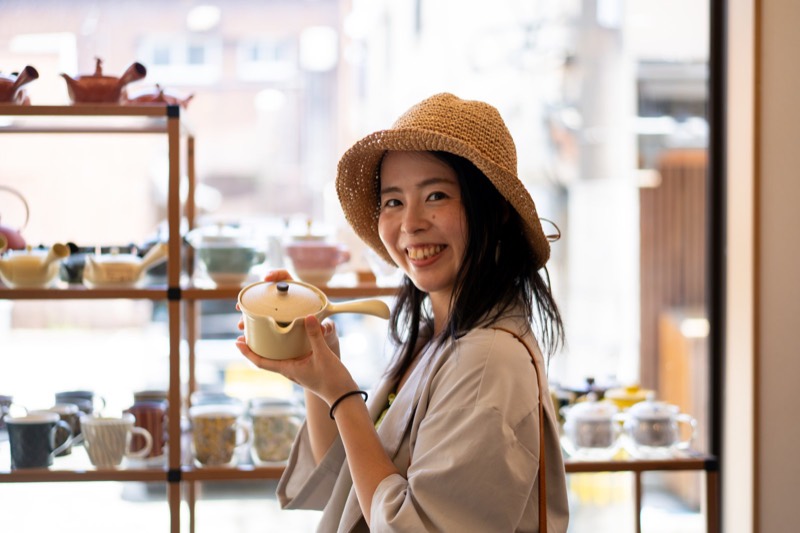 急須が並ぶお茶屋さんで、急須を手に取って笑う女性